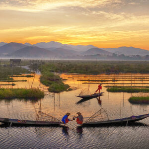 Traditional fishermen on Inle Lake at sunrise, with scenic mountains and floating gardens in the background.