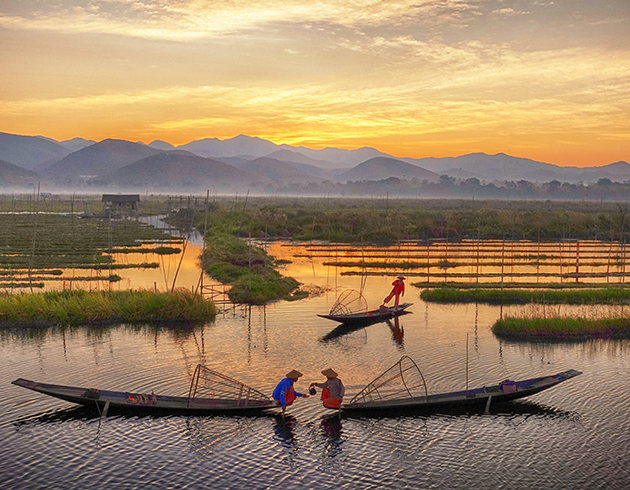 Traditional fishermen on Inle Lake at sunrise, with scenic mountains and floating gardens in the background.