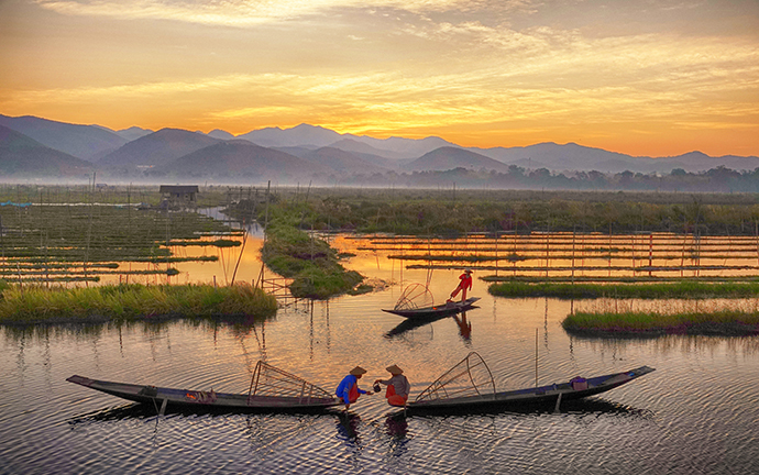 Traditional fishermen on Inle Lake at sunrise, with scenic mountains and floating gardens in the background