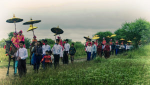 Traditional procession in Myanmar with locals dressed in vibrant attire, holding umbrellas, showcasing cultural richness during a Private Myanmar Photo Tour