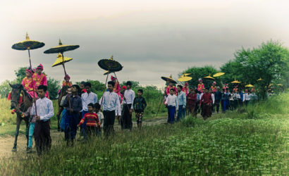 Traditional procession in Myanmar with locals dressed in vibrant attire, holding umbrellas, showcasing cultural richness during a Private Myanmar Photo Tour