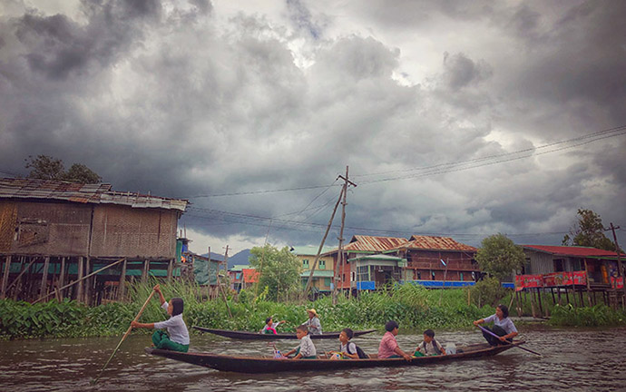 Local villagers paddling traditional wooden boats through the waterways of Inle Lake, Myanmar, under dramatic monsoon clouds.