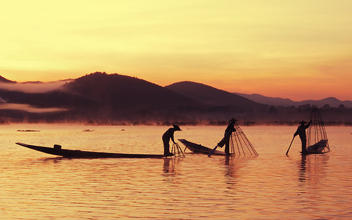 Traditional fishermen on Inle Lake casting their nets at sunrise, silhouetted against the calm waters and misty mountains.