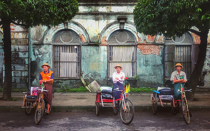 Three rickshaw drivers resting with their bikes in front of an old colonial building in Yangon, Myanmar.